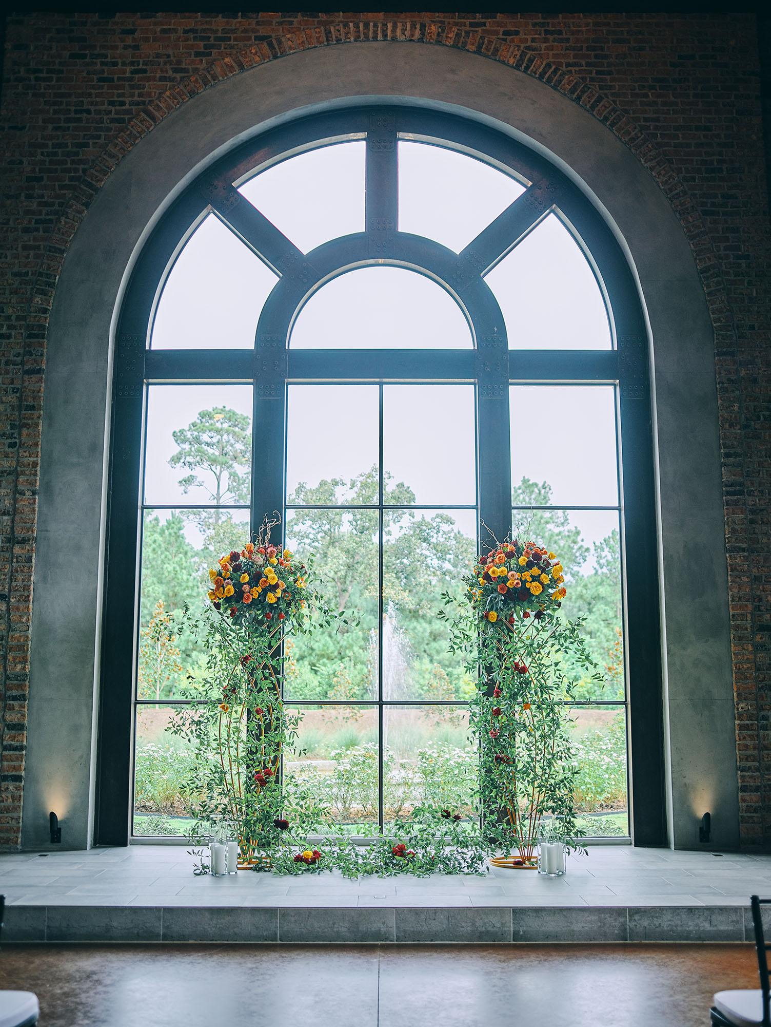 luxurious indoor wedding ceremony decor design, with a large red, yellow, and orange floral designs and a colorful bridal bouquet.