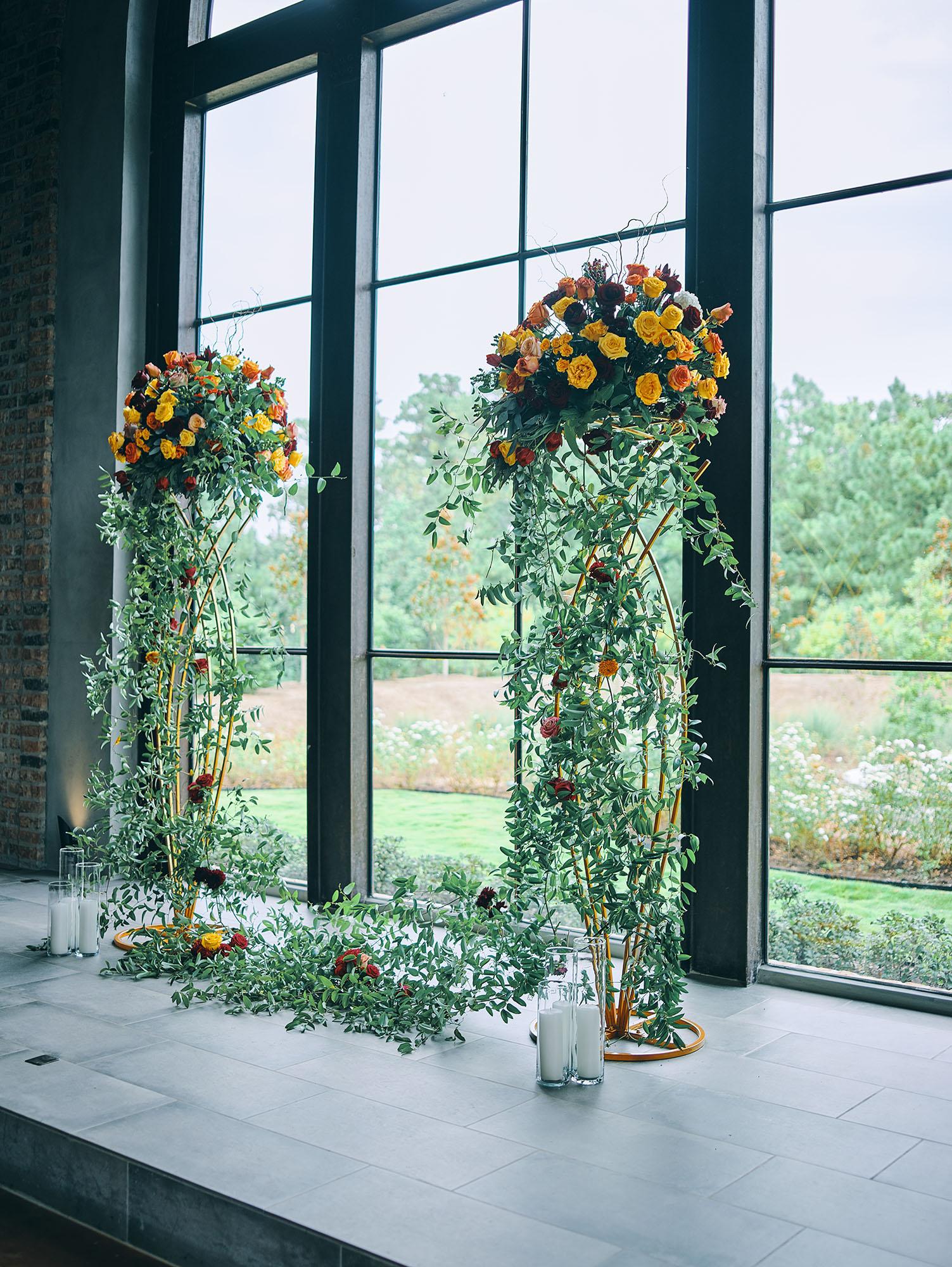 luxurious indoor wedding ceremony decor design, with a large red, yellow, and orange floral designs and a colorful bridal bouquet.