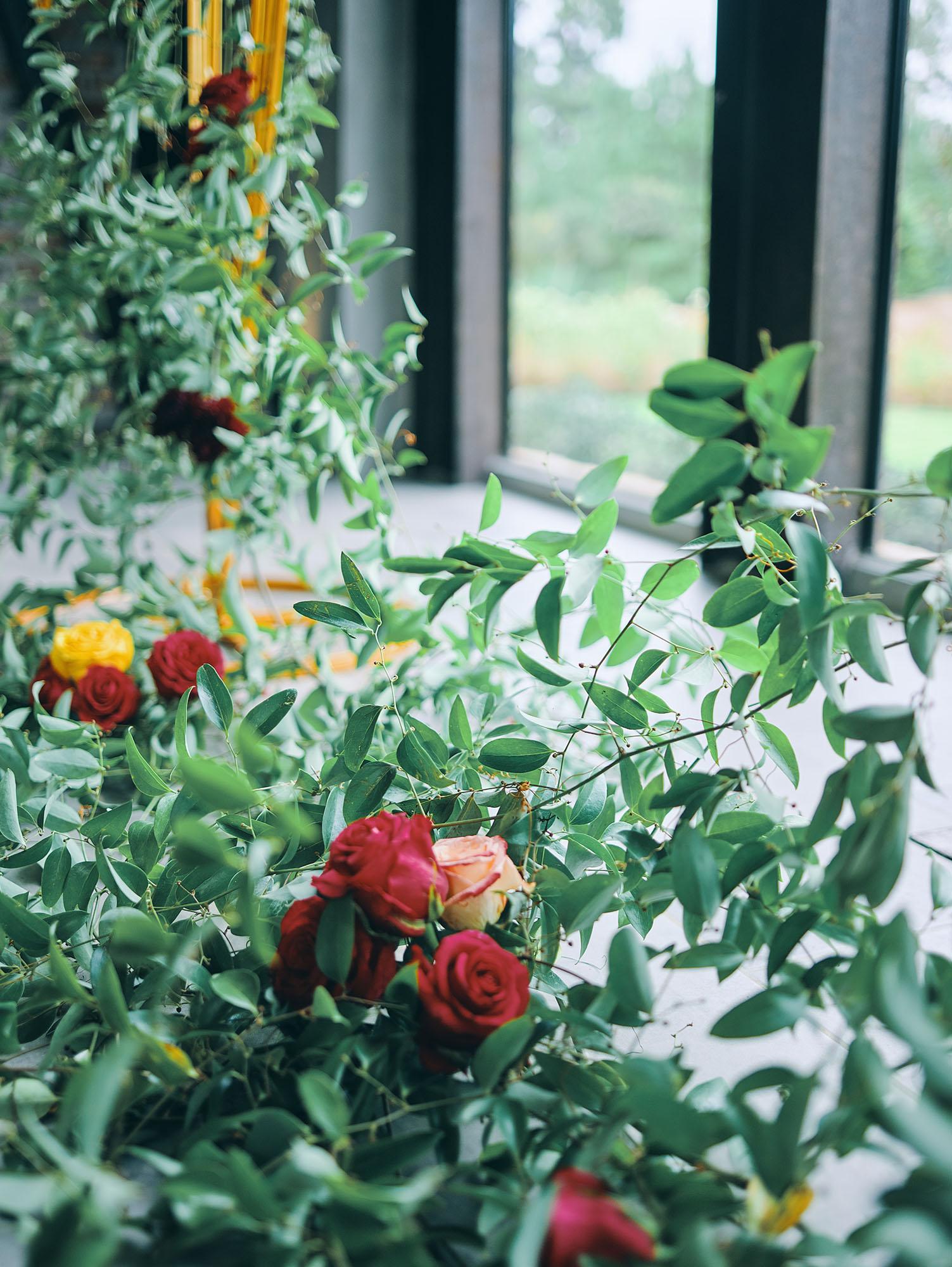 luxurious indoor wedding ceremony decor design, with a large red, yellow, and orange floral designs and a colorful bridal bouquet.