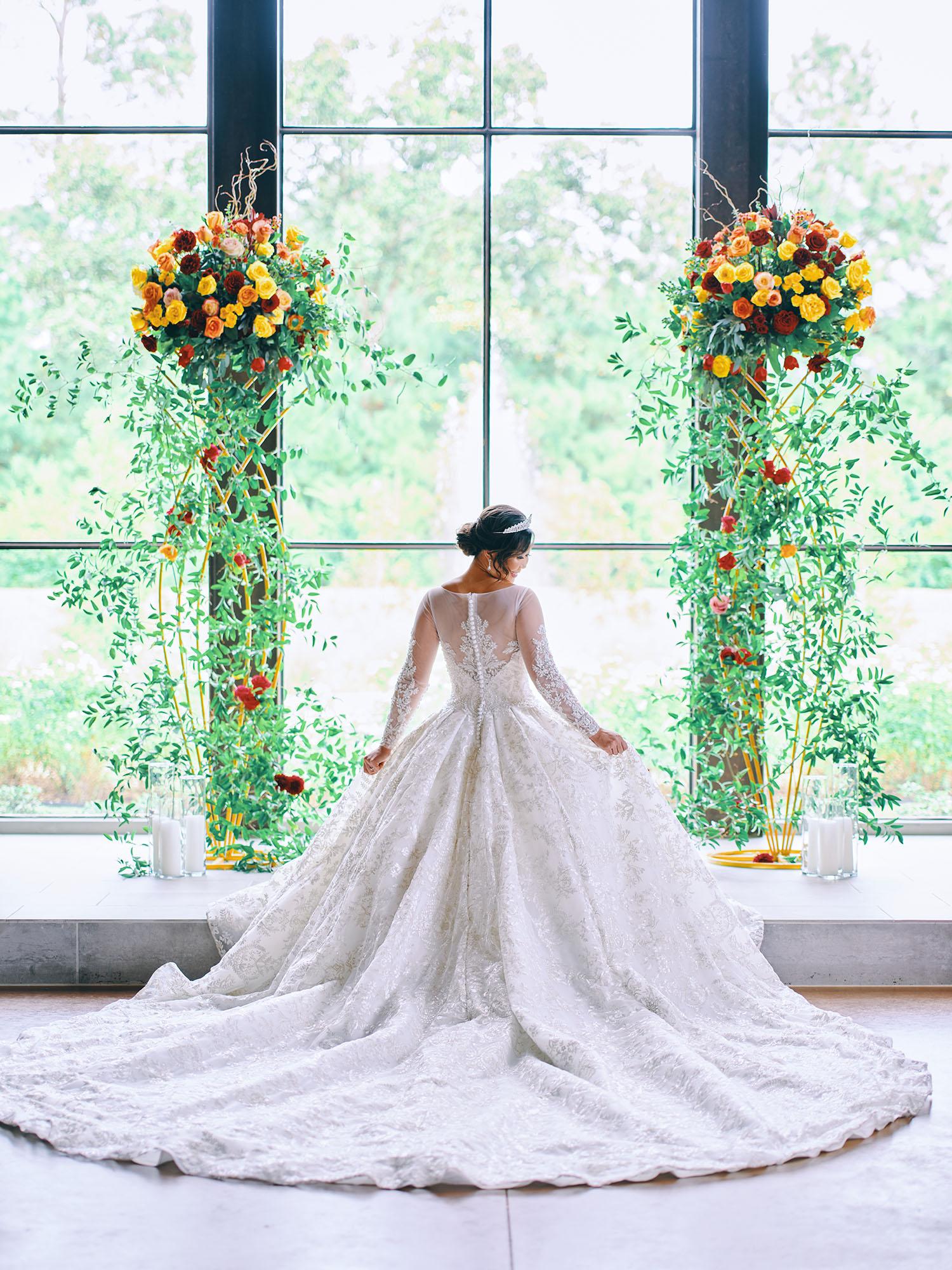 luxurious indoor wedding ceremony decor design, with a large red, yellow, and orange floral designs and a colorful bridal bouquet.