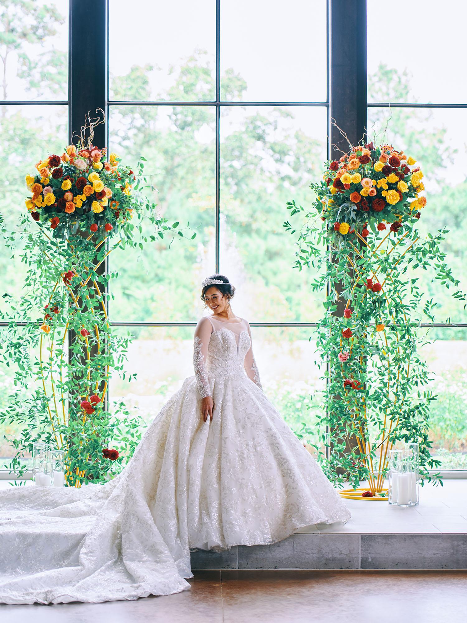 luxurious indoor wedding ceremony decor design, with a large red, yellow, and orange floral designs and a colorful bridal bouquet.