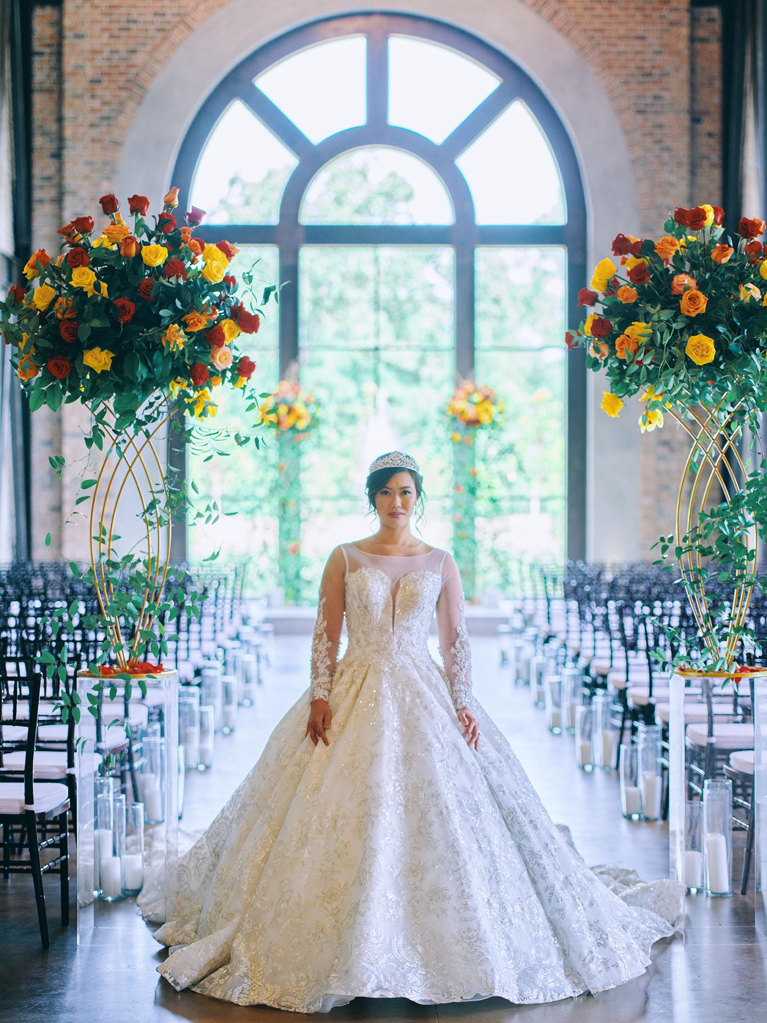 luxurious indoor wedding ceremony decor design, with a large red, yellow, and orange floral designs and a colorful bridal bouquet.