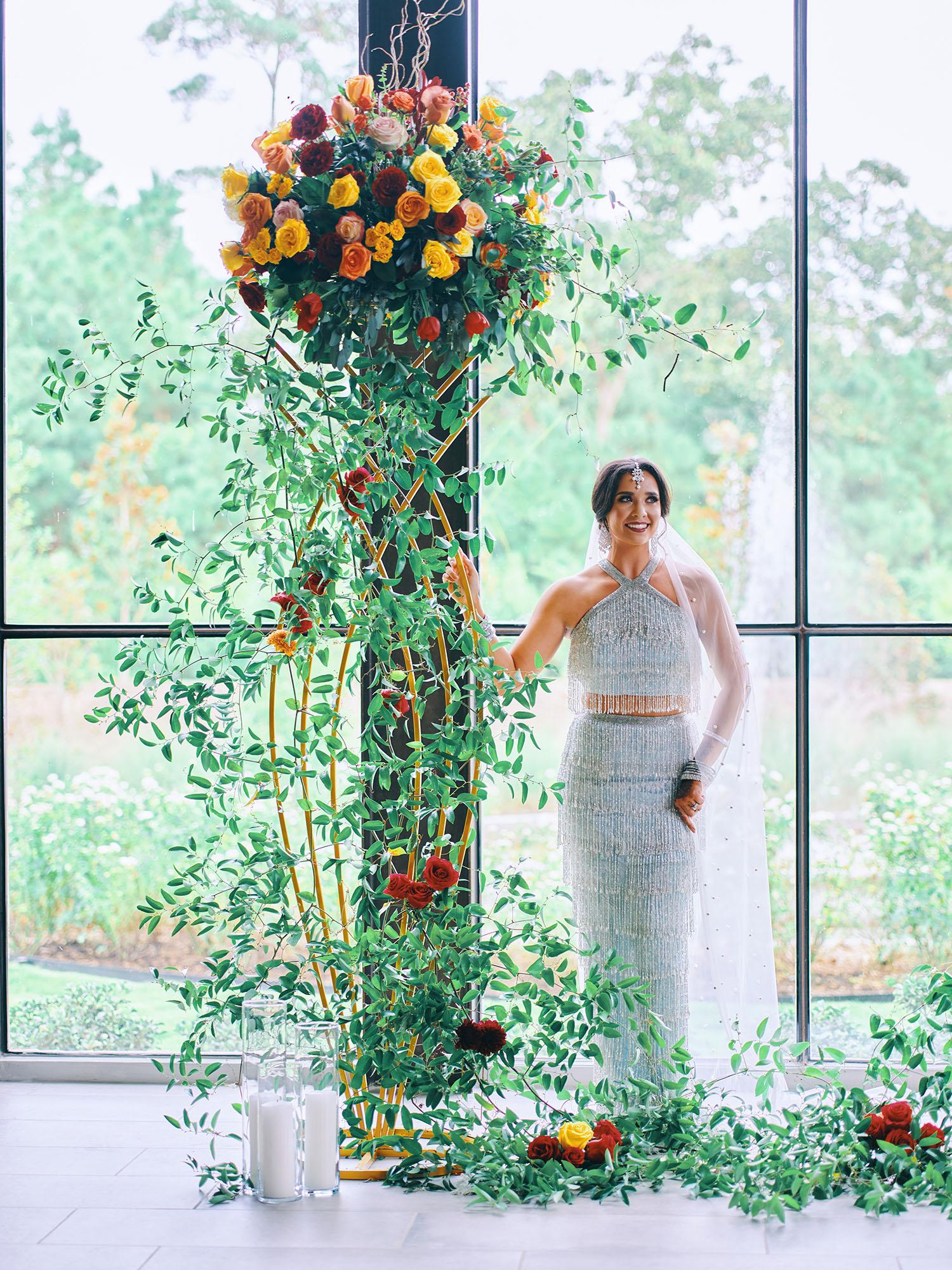 luxurious indoor wedding ceremony decor design, with a large red, yellow, and orange floral designs and a colorful bridal bouquet.