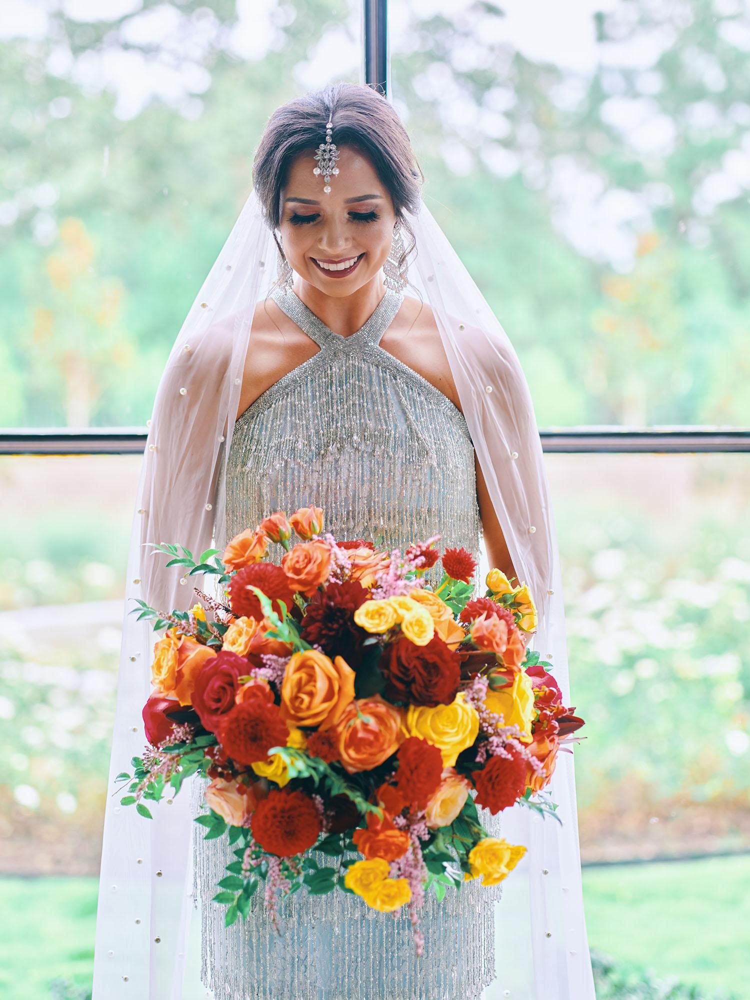 luxurious indoor wedding ceremony decor design, with a large red, yellow, and orange floral designs and a colorful bridal bouquet.