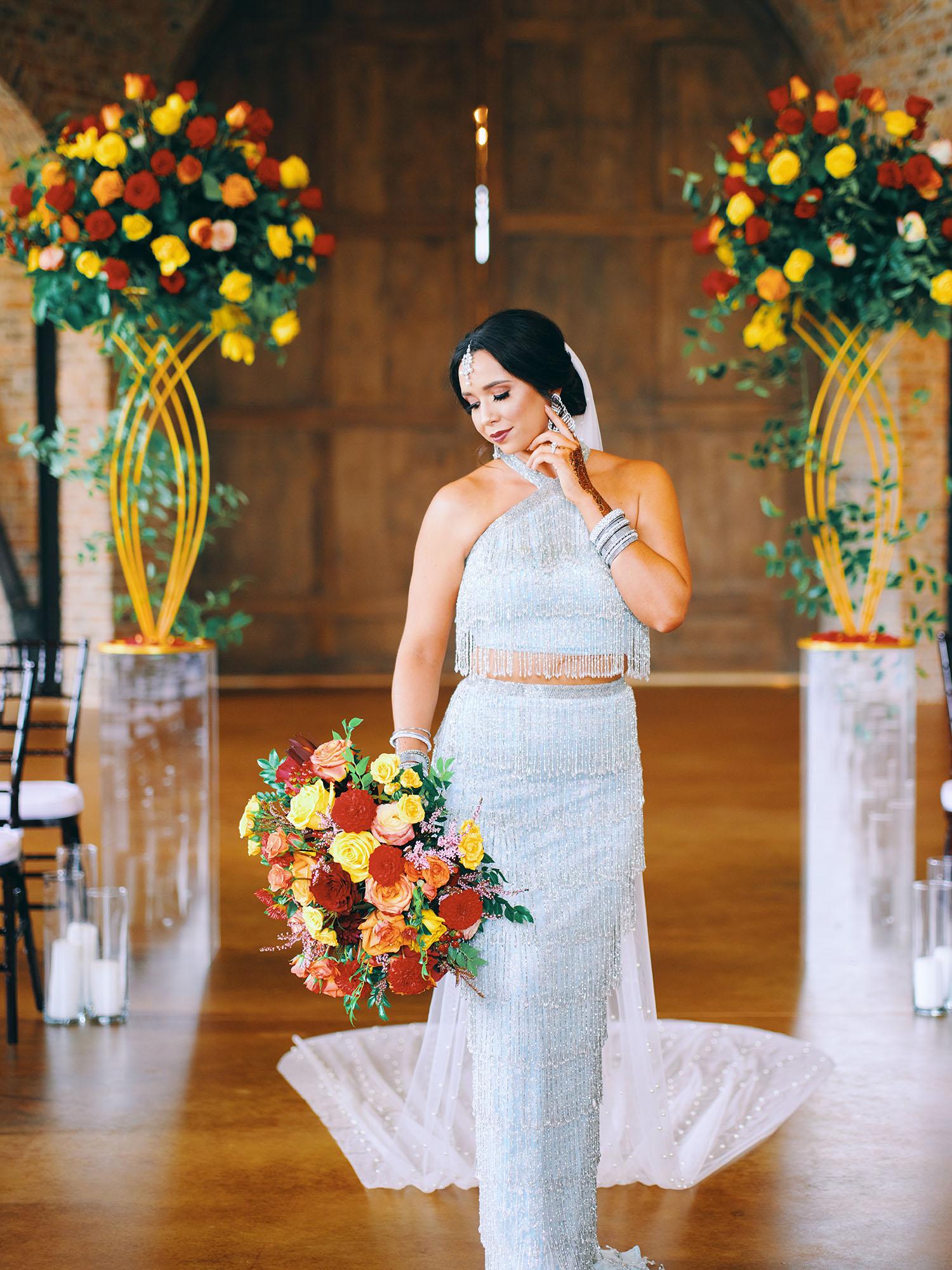 luxurious indoor wedding ceremony decor design, with a large red, yellow, and orange floral designs and a colorful bridal bouquet.
