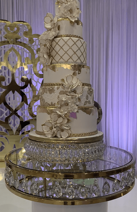 The reception decor featured gold crystal serpentine tables with floral runners, a white and gold dance floor with a custom monogram, a crystal gold cake table, and tall clear vase centerpieces.