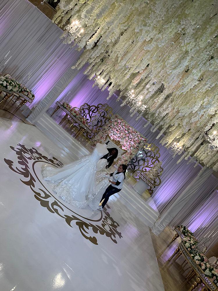 The reception decor featured gold crystal serpentine tables with floral runners, a white and gold dance floor with a custom monogram, a crystal gold cake table, and tall clear vase centerpieces.