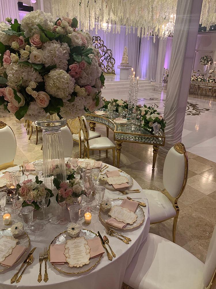 The reception decor featured gold crystal serpentine tables with floral runners, a white and gold dance floor with a custom monogram, a crystal gold cake table, and tall clear vase centerpieces.