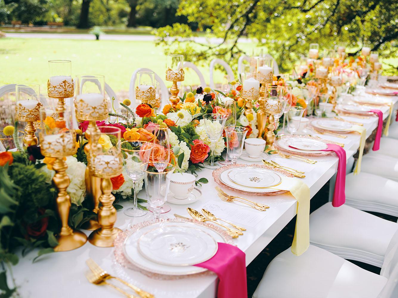 outdoor wedding reception - white chairs - pink napkins, charger plates, gold tableware, floral table runner, wedding cake, pink, yellow, orange, bouquet, houstonian, royal luxury events