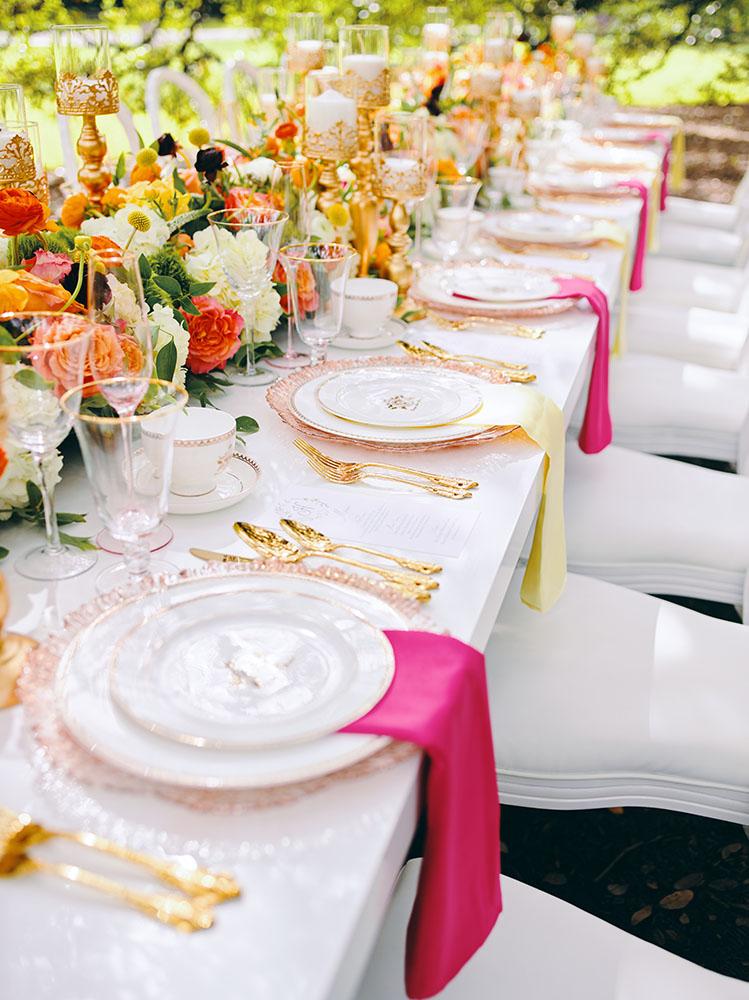 outdoor wedding reception - white chairs - pink napkins, charger plates, gold tableware, floral table runner, wedding cake, pink, yellow, orange, bouquet, houstonian, royal luxury events