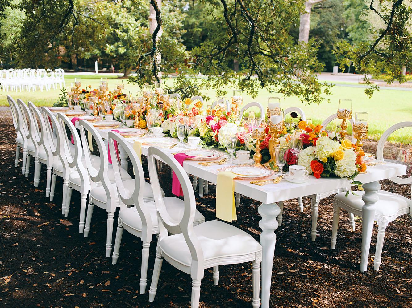 outdoor wedding reception - white chairs - pink napkins, charger plates, gold tableware, floral table runner, wedding cake, pink, yellow, orange, bouquet, houstonian, royal luxury events