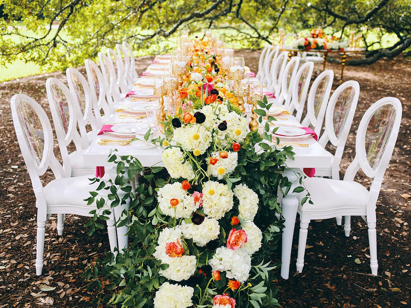 outdoor wedding reception - white chairs - pink napkins, charger plates, gold tableware, floral table runner, wedding cake, pink, yellow, orange, bouquet, houstonian, royal luxury events