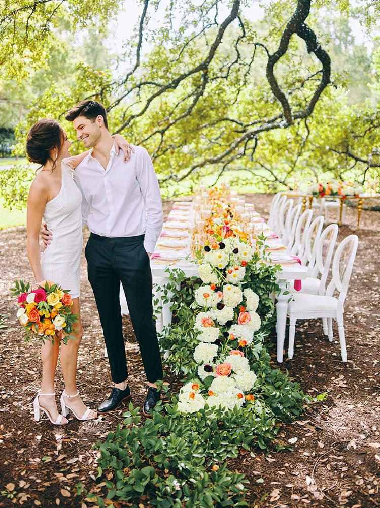 outdoor wedding reception - white chairs - pink napkins, charger plates, gold tableware, floral table runner, wedding cake, pink, yellow, orange, bouquet, houstonian, royal luxury events