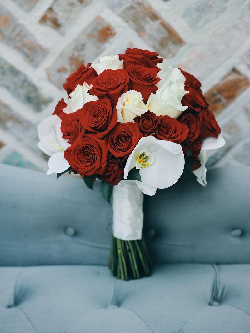 luxurious indoor wedding reception decor design, with red, and white floral designs, gold and white curved tables, gold chairs, and a stunning bride and bridal bouquet.