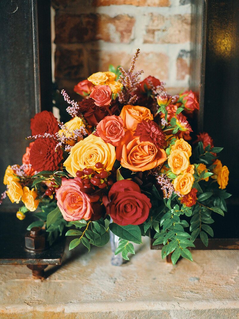 luxurious indoor wedding reception decor design, with red, yellow and orange floral designs, gold and black chairs, rectangular table, and a stunning bride and bridal bouquet.