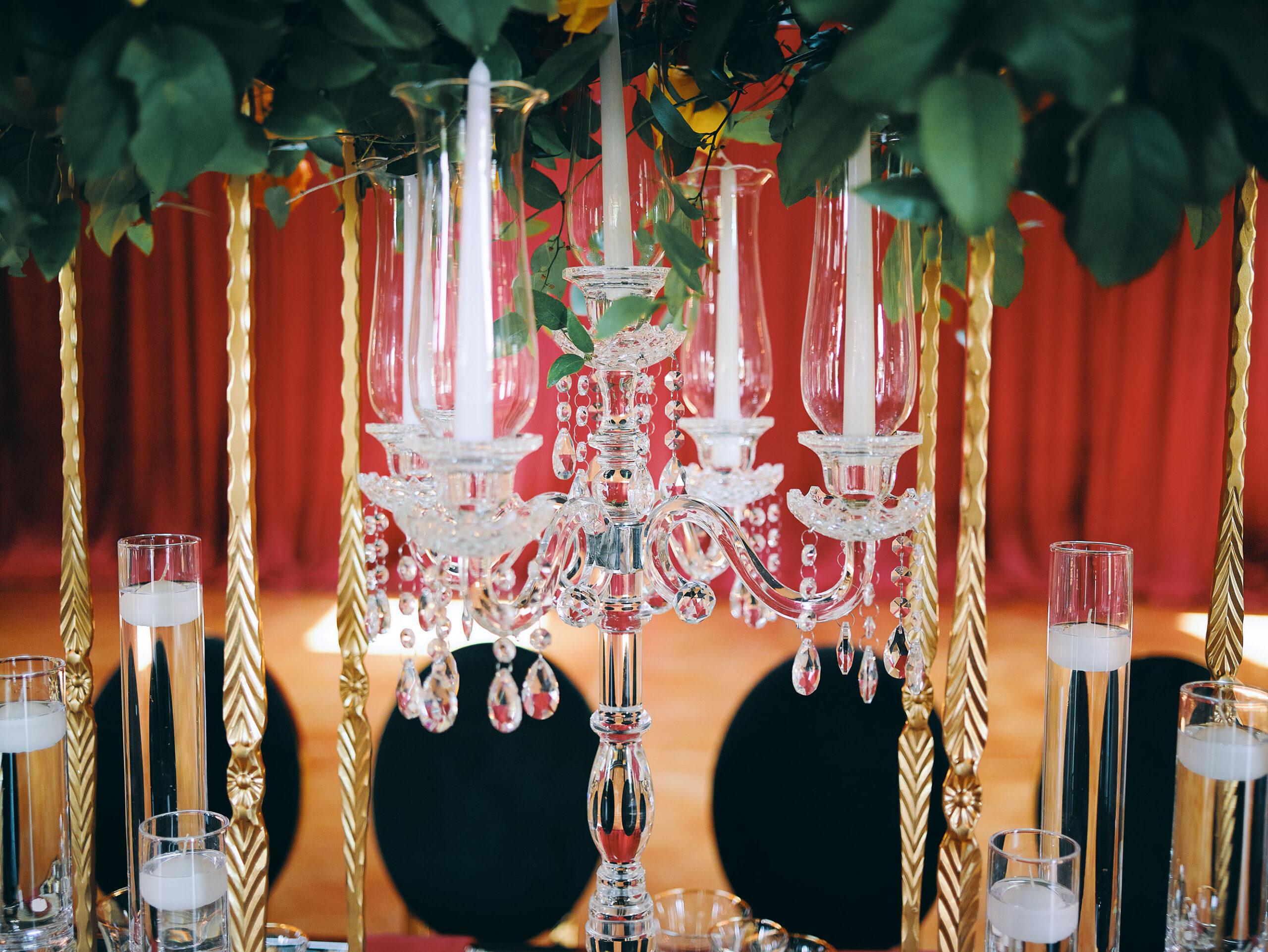 luxurious indoor wedding reception decor design, with red, yellow and orange floral designs, gold and black chairs, rectangular table, and a stunning bride and bridal bouquet.