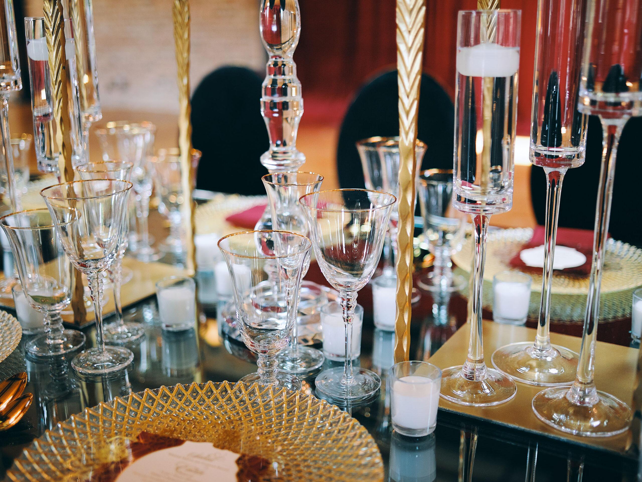 luxurious indoor wedding reception decor design, with red, yellow and orange floral designs, gold and black chairs, rectangular table, and a stunning bride and bridal bouquet.