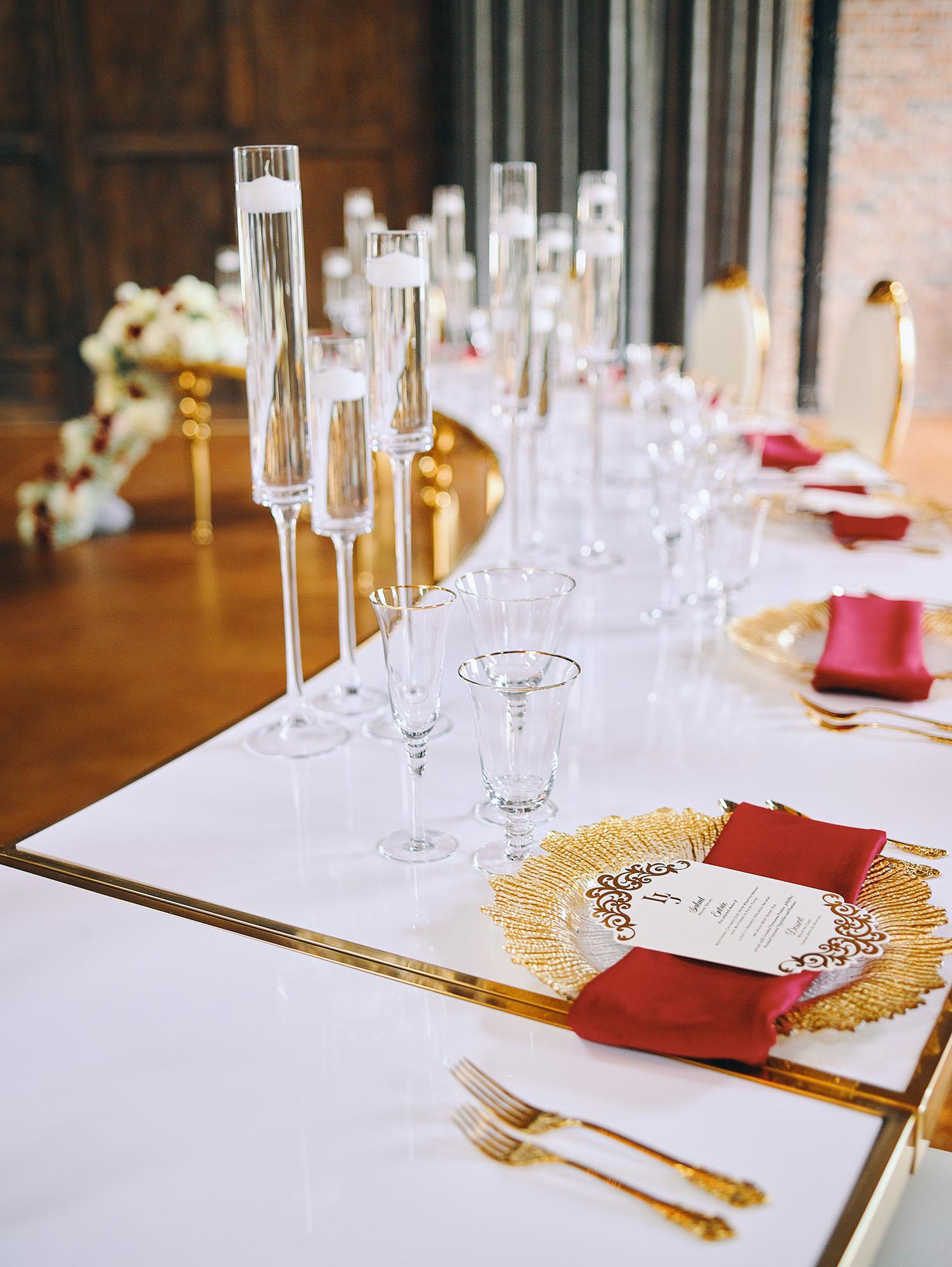 luxurious indoor wedding reception decor design, with red, and white floral designs, gold and white curved tables, gold chairs, and a stunning bride and bridal bouquet.