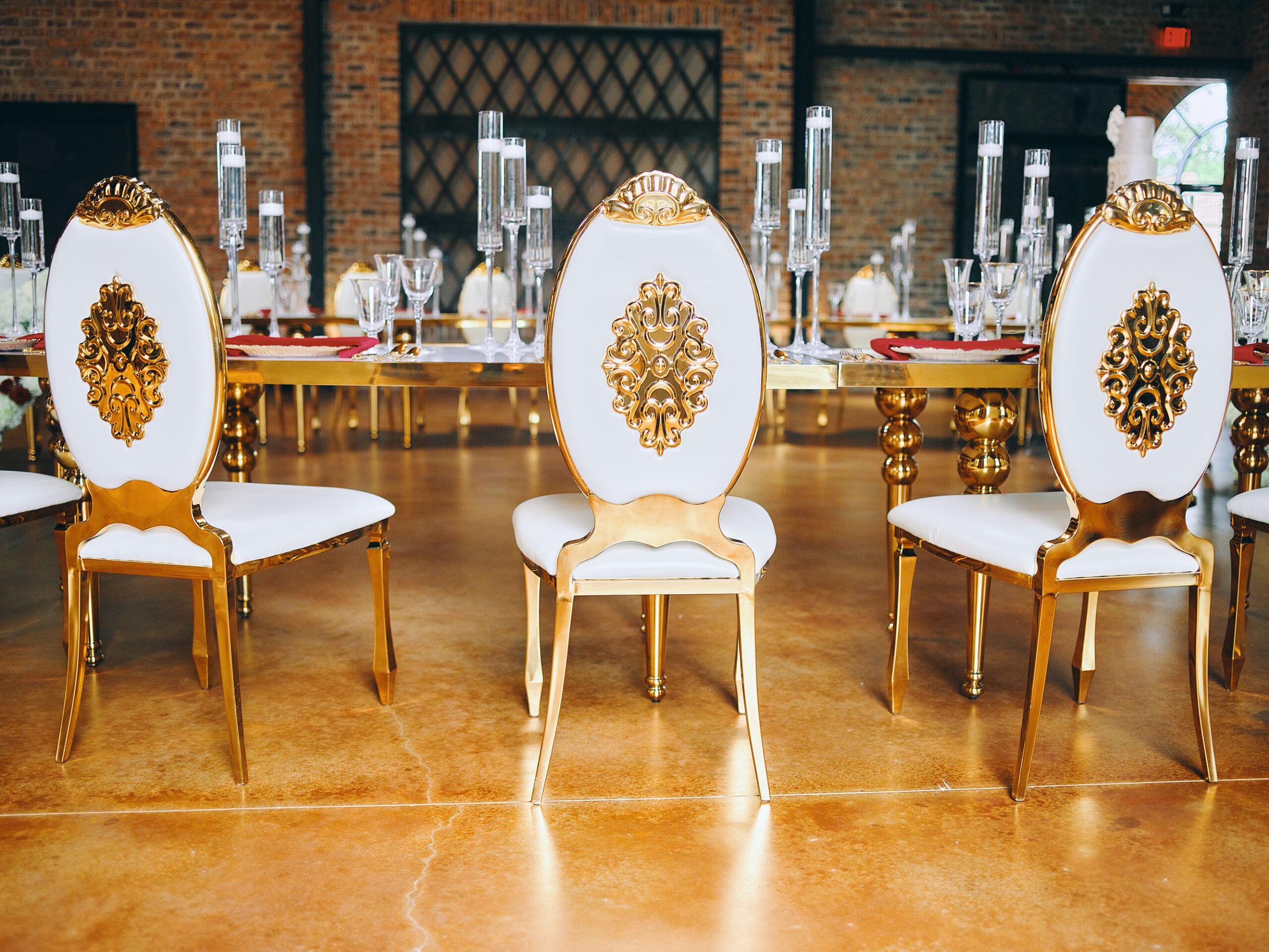 luxurious indoor wedding reception decor design, with red, and white floral designs, gold and white curved tables, gold chairs, and a stunning bride and bridal bouquet.