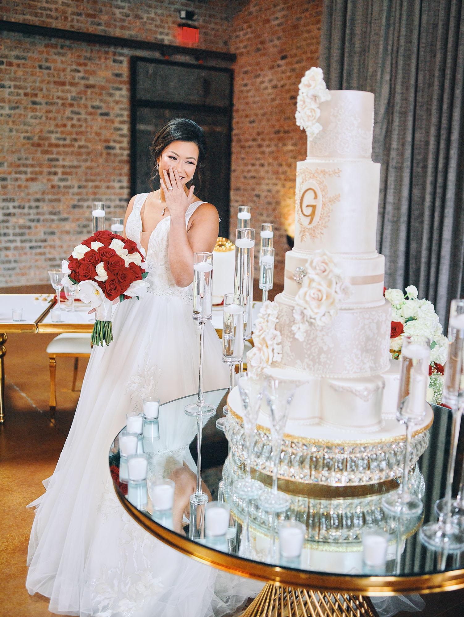 luxurious indoor wedding reception decor design, with red, and white floral designs, gold and white curved tables, gold chairs, and a stunning bride and bridal bouquet.