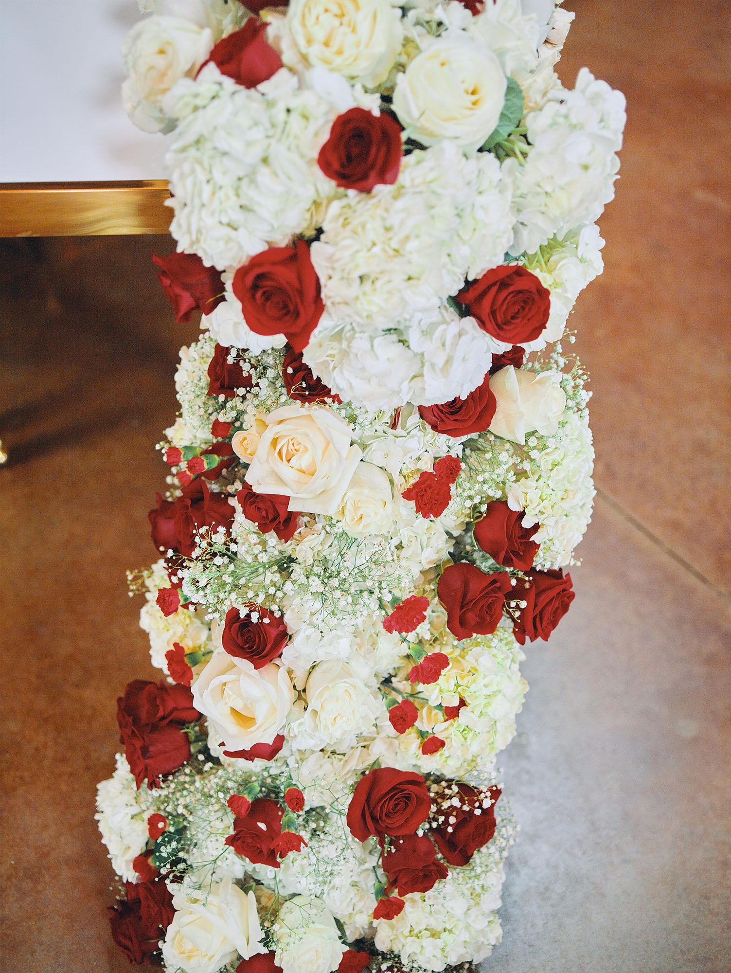 luxurious indoor wedding reception decor design, with red, and white floral designs, gold and white curved tables, gold chairs, and a stunning bride and bridal bouquet.