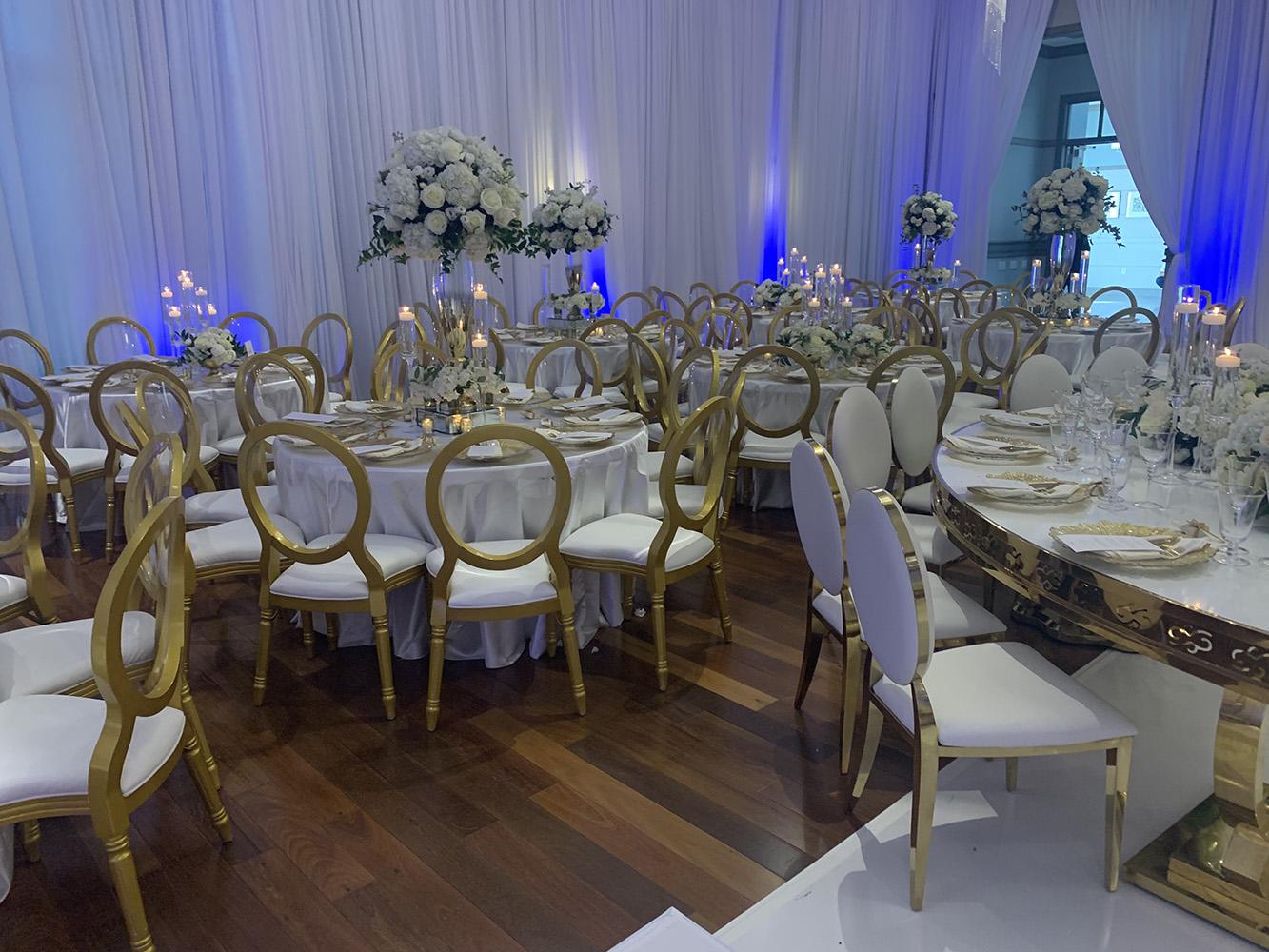 NOAH’s Event Venue. Featuring gold and white wedding decor, with blue uplighting.