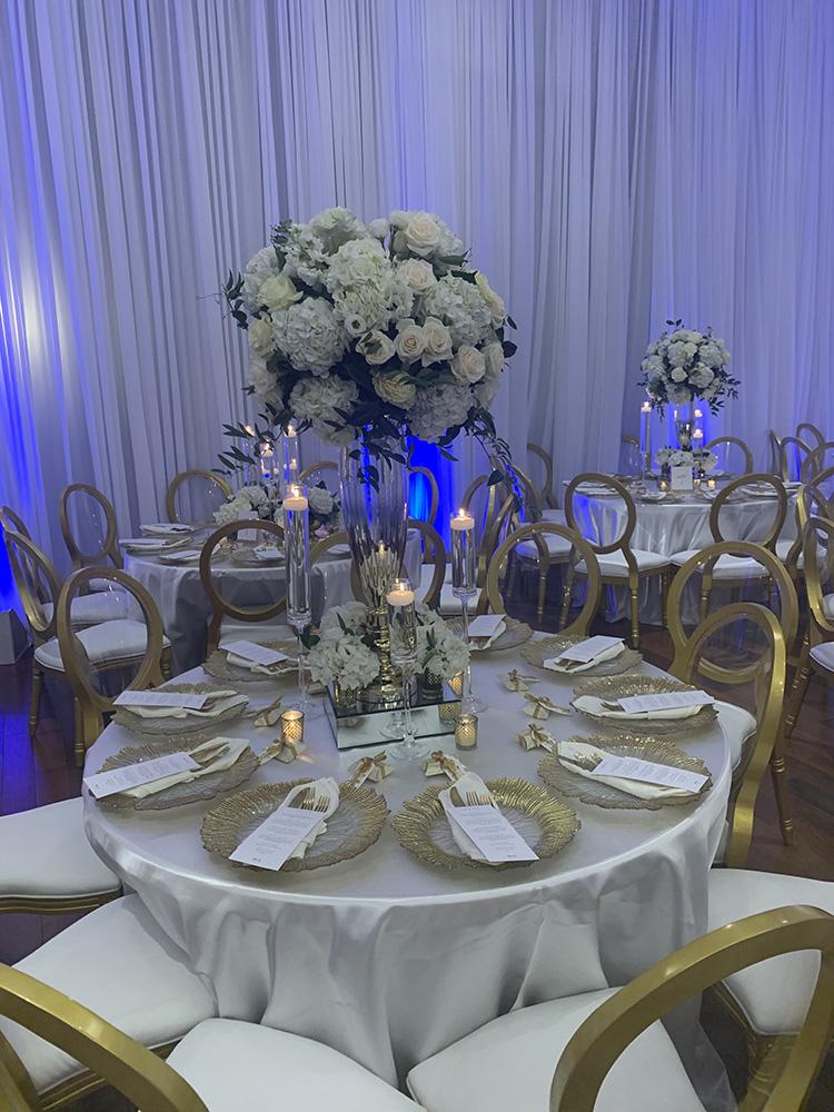 NOAH’s Event Venue. Featuring gold and white wedding decor, with blue uplighting.