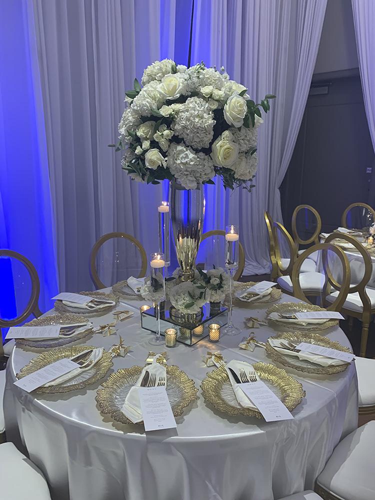 NOAH’s Event Venue. Featuring gold and white wedding decor, with blue uplighting.
