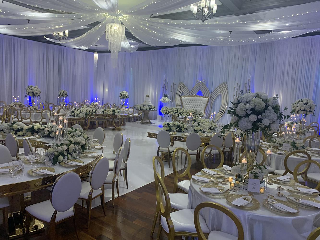 NOAH’s Event Venue. Featuring gold and white wedding decor, with blue uplighting.