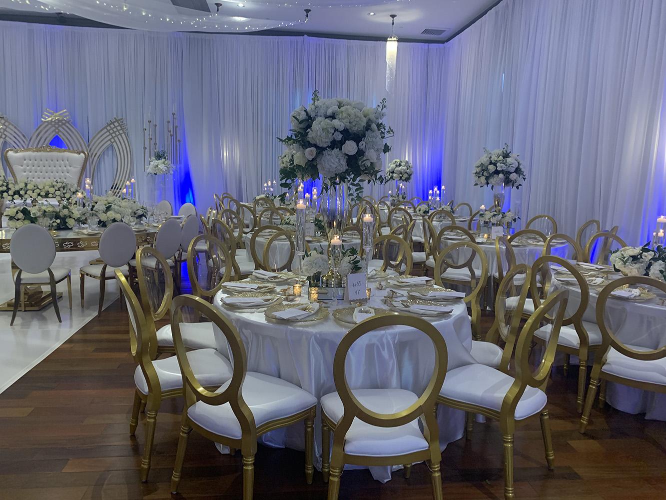 NOAH’s Event Venue. Featuring gold and white wedding decor, with blue uplighting.