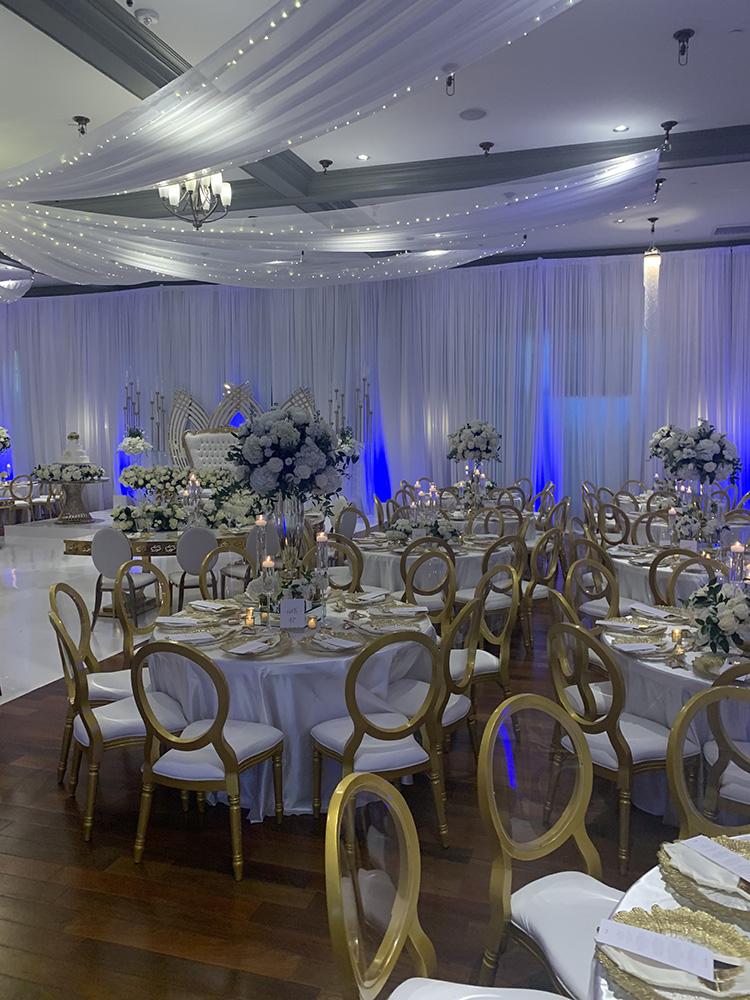 NOAH’s Event Venue. Featuring gold and white wedding decor, with blue uplighting.